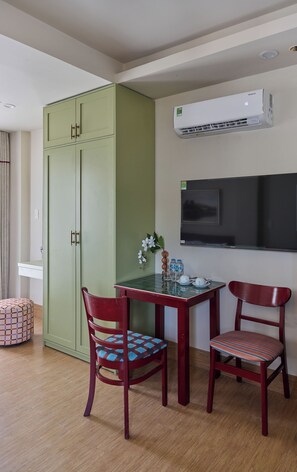 A room with a green wardrobe, two wooden chairs, a small table with a vase and bottles, and a mounted air conditioner. - LangX Heaven Hotel & Apartment (Ngu Hanh Son)