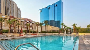 A hotel with a swimming pool, palm trees, and modern buildings in the background.