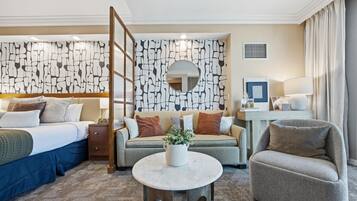 Ein Hotelzimmer mit einem Bett, einer Couch, einem Sessel, einem kleinen Tisch mit einer Vase und einer Wand mit geometrischem Muster.