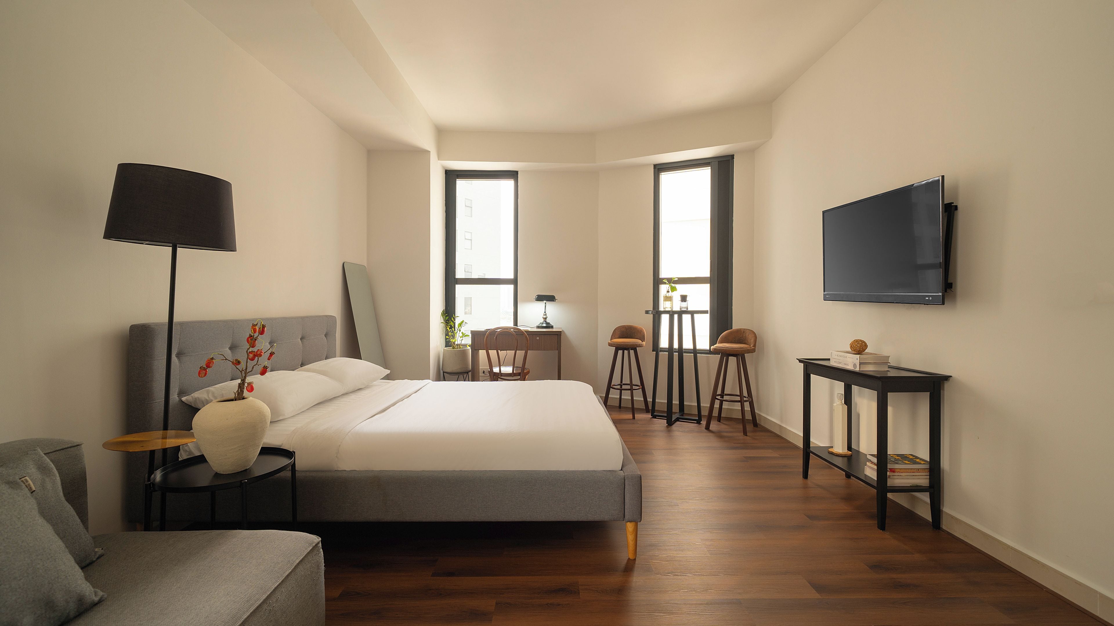 Une chambre moderne comprenant un lit, une table de chevet, une lampe, une chaise, un téléviseur et un coin bureau avec une chaise et un tabouret.