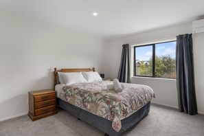 A bedroom with a bed, a nightstand, a window with curtains, and a view of the outside. - The Tin Hutt, Kinloch (Kinloch)