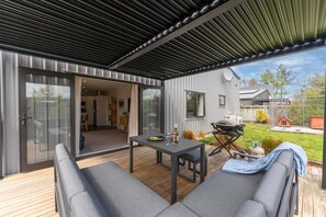 Eine moderne Terrassenanlage im Freien mit Tisch, Sitzgelegenheiten, einem Grill und Blick auf den Garten.