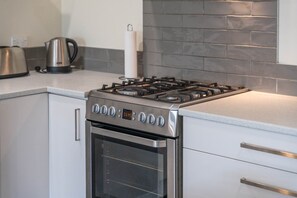 Cozinha moderna com fogão a gás de aço inoxidável, forno embutido e painel de backsplash em azulejo cinza.