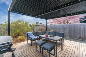 A covered outdoor patio with a barbecue grill, a dining table with chairs, and a seating area. - The Tin Hutt, Kinloch (Kinloch)