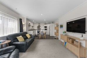 Ein modernes Wohnzimmer mit einer schwarzen Ledersofa, einem Flachbildfernseher und einem Essbereich mit Tisch und Stühlen.