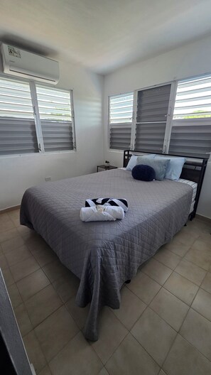 Quarto com cama, almofadas, mesa de cabeceira e ar condicionado.