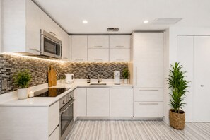 Una cocina moderna con armarios blancos, un salpicadero de azulejos negros y grises, electrodomésticos de acero inoxidable y una planta en maceta.