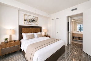 A modern hotel room with a large bed, bedside tables with lamps, a headboard, a painting, a wardrobe, and a bathroom visible through an open door. - Luxury Apt in the Heart of Brickell – 44th Floor (Miami)