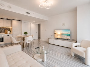 A modern living room with a flat-screen TV, a dining area with a table and chairs, and a kitchen with cabinets and a countertop. - Luxury Apt in the Heart of Brickell – 44th Floor (Miami)