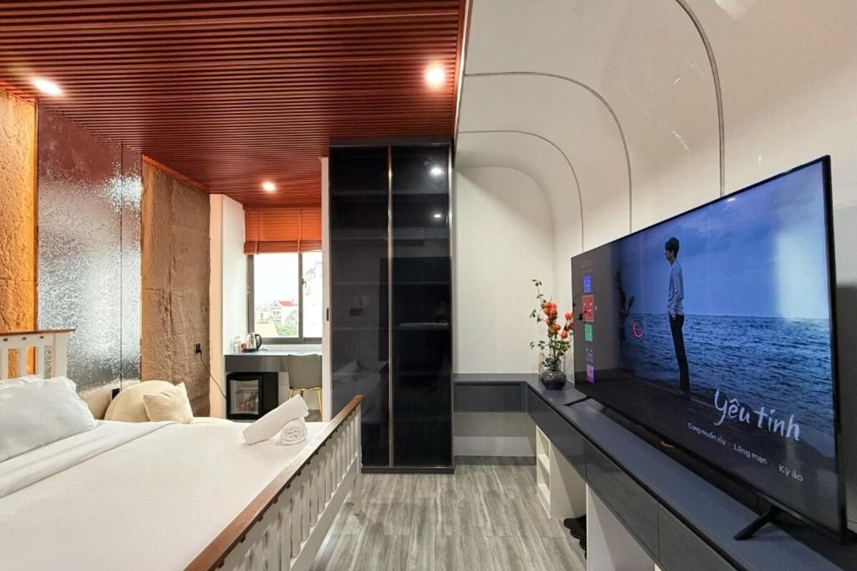 A modern hotel room with a large flat-screen TV, a bed, a seating area, and a view of the sea.