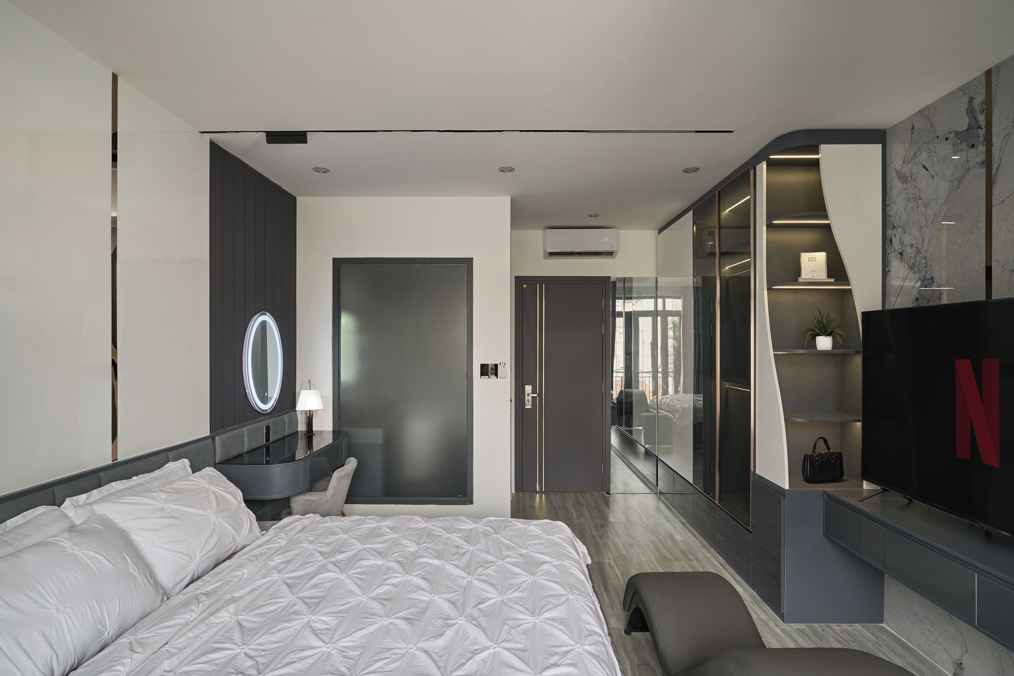 A modern hotel room with a large bed, a vanity with a mirror, a TV, and a wardrobe.