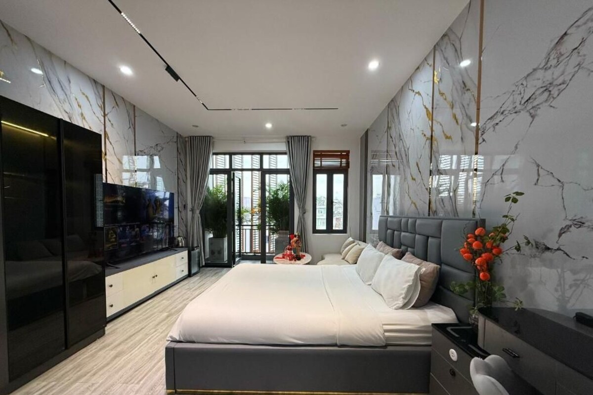 A modern bedroom with a large bed, built-in TV, and a marble wall.