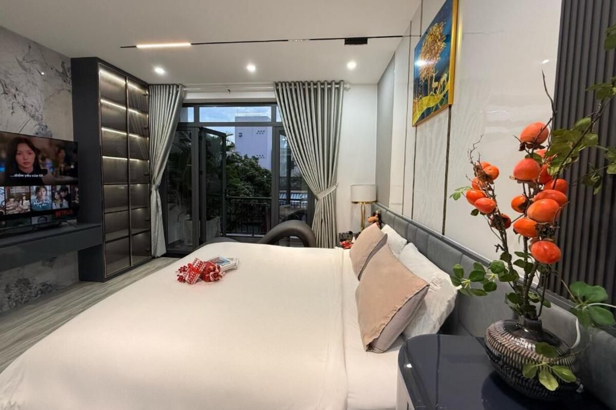 A modern hotel room with a bed, a TV, a plant, and a view of the outdoors.