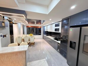 A modern kitchen with a central island, stainless steel appliances, and a dining area with chairs. - Solana Garden Hotel by Urban B (Go Vap)