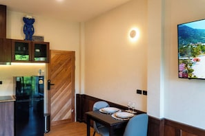 Une cuisine compacte équipée d’un réfrigérateur, d’un four à micro-ondes et d’un meuble en bois. On y trouve un coin repas avec une table pour deux personnes, et un téléviseur fixé au mur qui diffuse une vue panoramique.