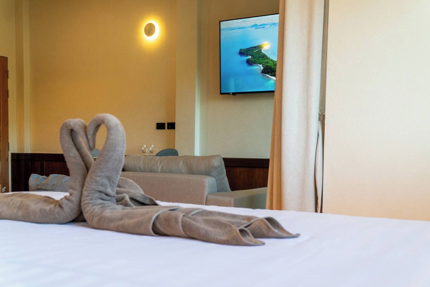 A hotel room with a bed, a sofa, a television on the wall, and a painting of a landscape.