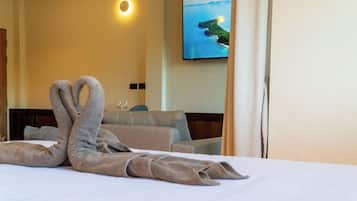 A hotel room with a bed, a sofa, a television on the wall, and a painting of a landscape.