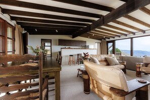 A spacious living area with a wooden dining table, a sofa, and a kitchen in the background.
