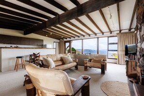 Amplia sala de estar con techos altos, un conjunto de sofás, una mesa de centro y vistas al exterior.