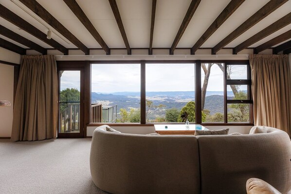 Una sala de estar con sofá, una mesa de centro y vistas a un paisaje montañoso a través de amplios ventanales.
