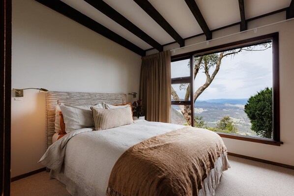 A bedroom with a large window, a bed with multiple pillows, and a view of the outdoors.
