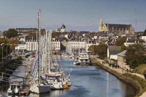 A harbor with boats docked along the waterfront, a prominent church in the background, and a pedestrian walkway alongside the water. - From Locmaria - LA CHAPELLE NEUVE (LA CHAPELLE NEUVE)
