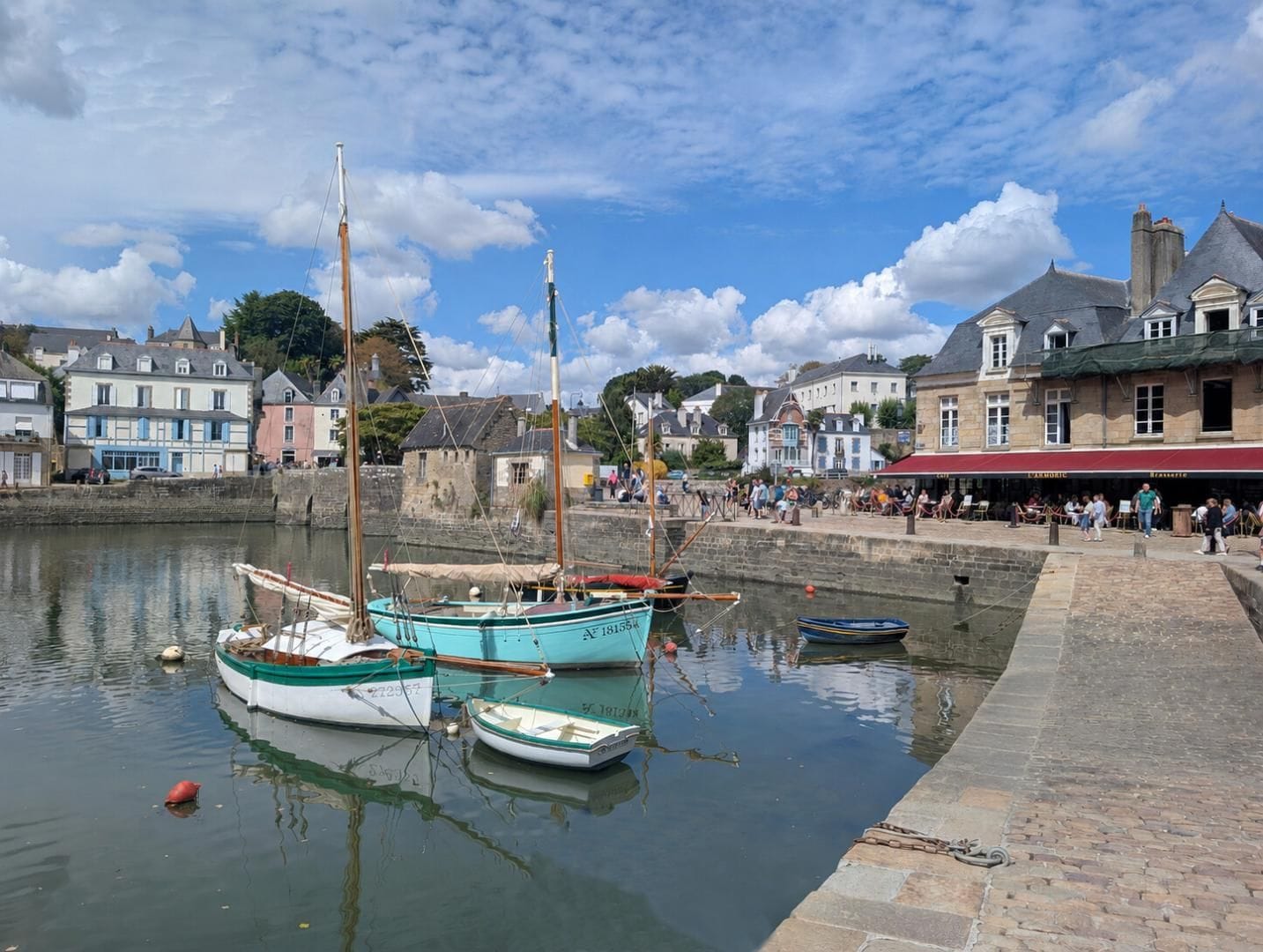 A harbor with boats docked, a stone quay, and buildings with commercial establishments.