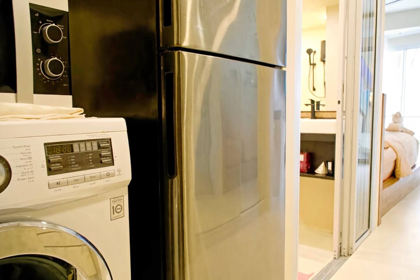 Une cuisine compacte équipée d’un réfrigérateur en acier inoxydable, d’un lave-linge et d’un four à micro-ondes.