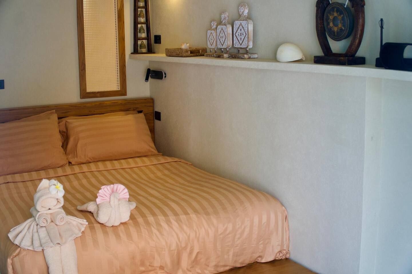 Un lit bien fait, avec une couvre-lit à rayures, deux serviettes enroulées et un objet décoratif posé sur la tête de lit.