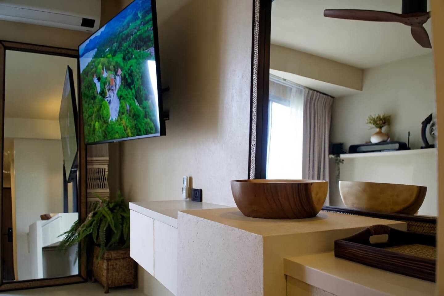 Een moderne keuken met een grote flatscreentelevisie, een houten kom op het aanrecht en een potplant.