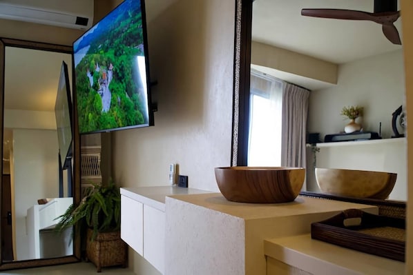 Une cuisine moderne avec un grand téléviseur à écran plat, un saladier en bois posé sur le plan de travail et une plante en pot.