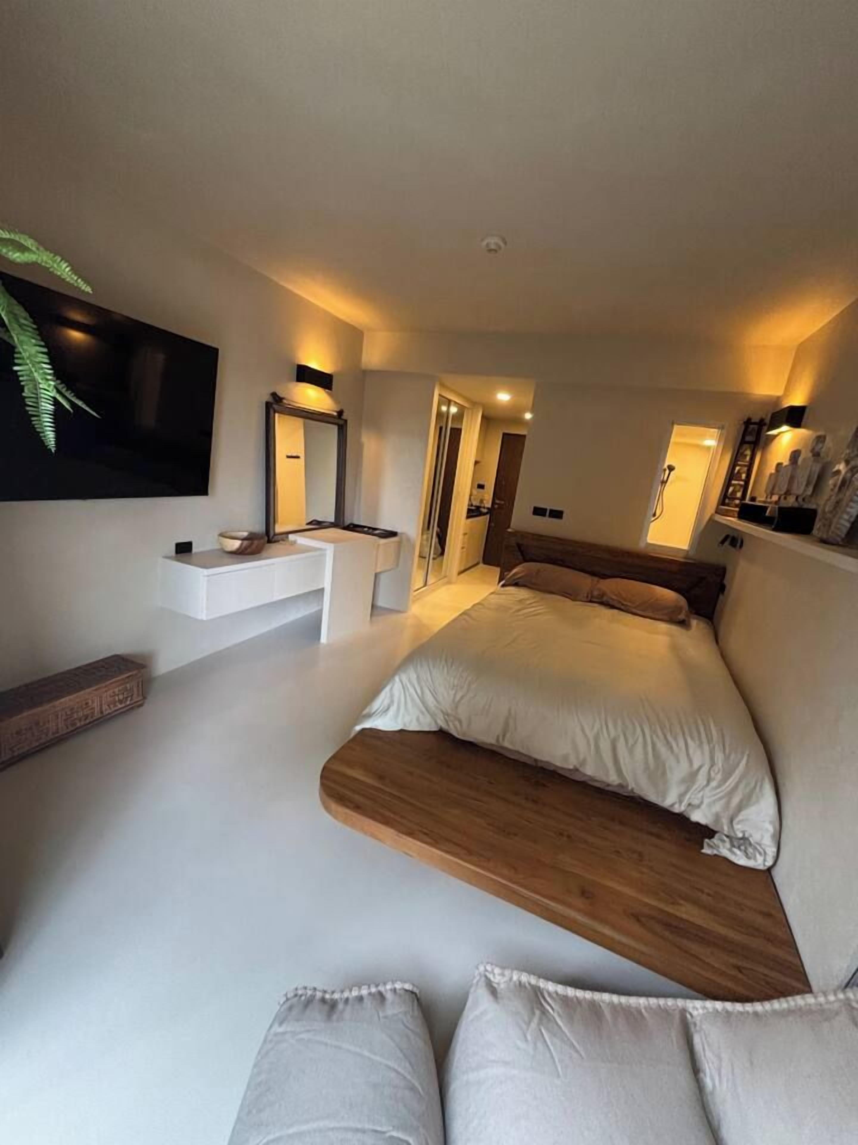 Ein modernes Schlafzimmer mit einem Bett, Nachttischen, einem an der Wand montierten Fernseher und einem Spiegel.