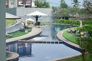 Une piscine au design incurvé, entourée de chaises longues et de parasols, ainsi qu’un petit espace avec un jacuzzi.
