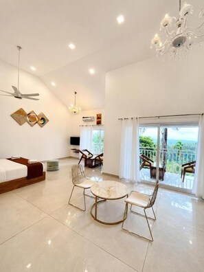 A modern hotel room with a bed, a dining table with chairs, a chandelier, and a balcony with a view. - Skybz Munnar (Devikolam)