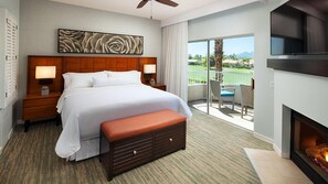 Ein Hotelzimmer mit einem großen Bett, einem Holzkopfteil, einem Flachbildfernseher, einem Kamin, einem Balkon mit Blick auf einen Golfplatz und einem Deckenventilator.