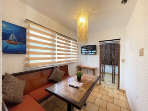 Una habitación con un banco de madera, una mesa con una planta y un televisor montado en la pared.