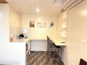 Cocina compacta con lavamanos, un pequeño comedor con una silla y un equipo de aire acondicionado de pared.