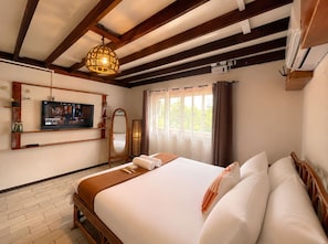 A hotel room with a bed, a television, a mirror, and a window with curtains. - Galera Lodge & Cafe (Puerto Galera)