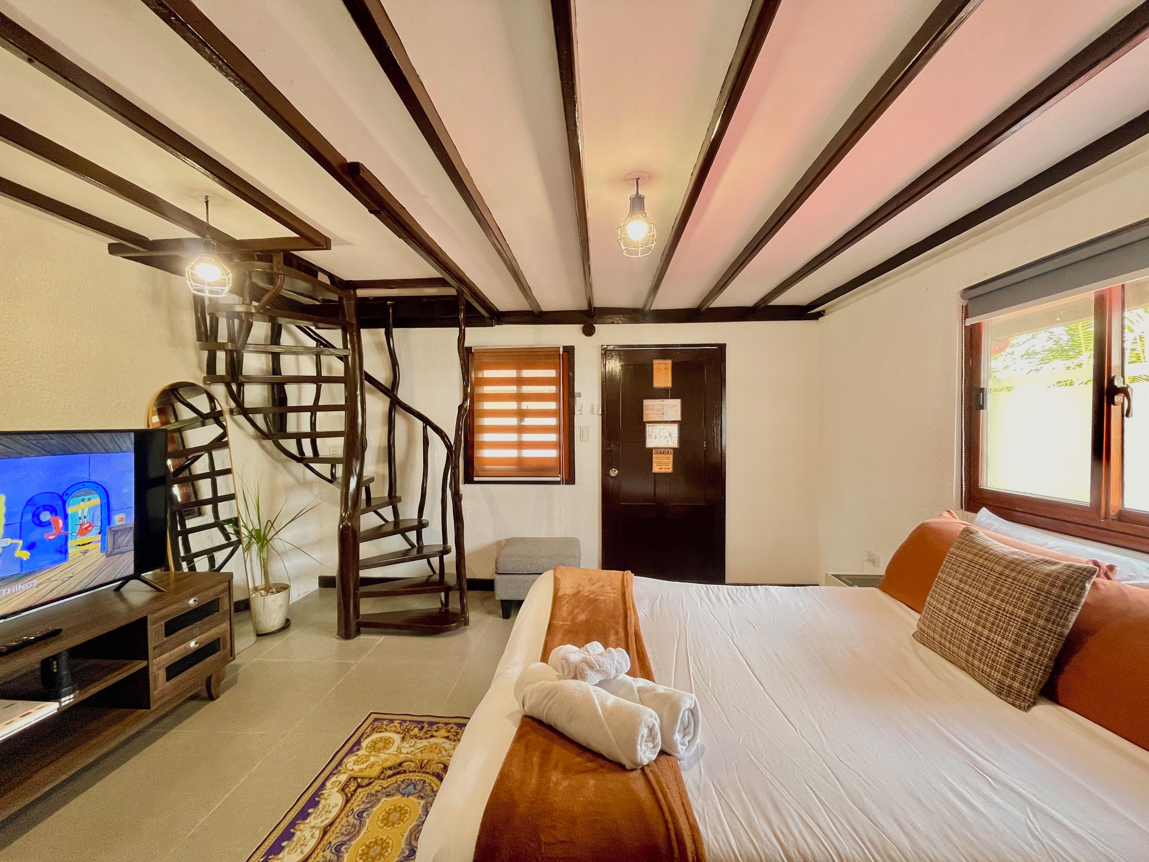 Ein Schlafzimmer mit einem Bett, einem Fernseher, einer Treppe und einem Fenster.