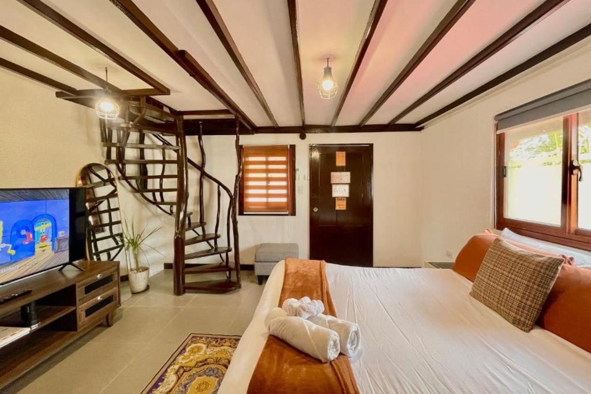 A hotel room with a bed, a TV, a staircase, and a door.