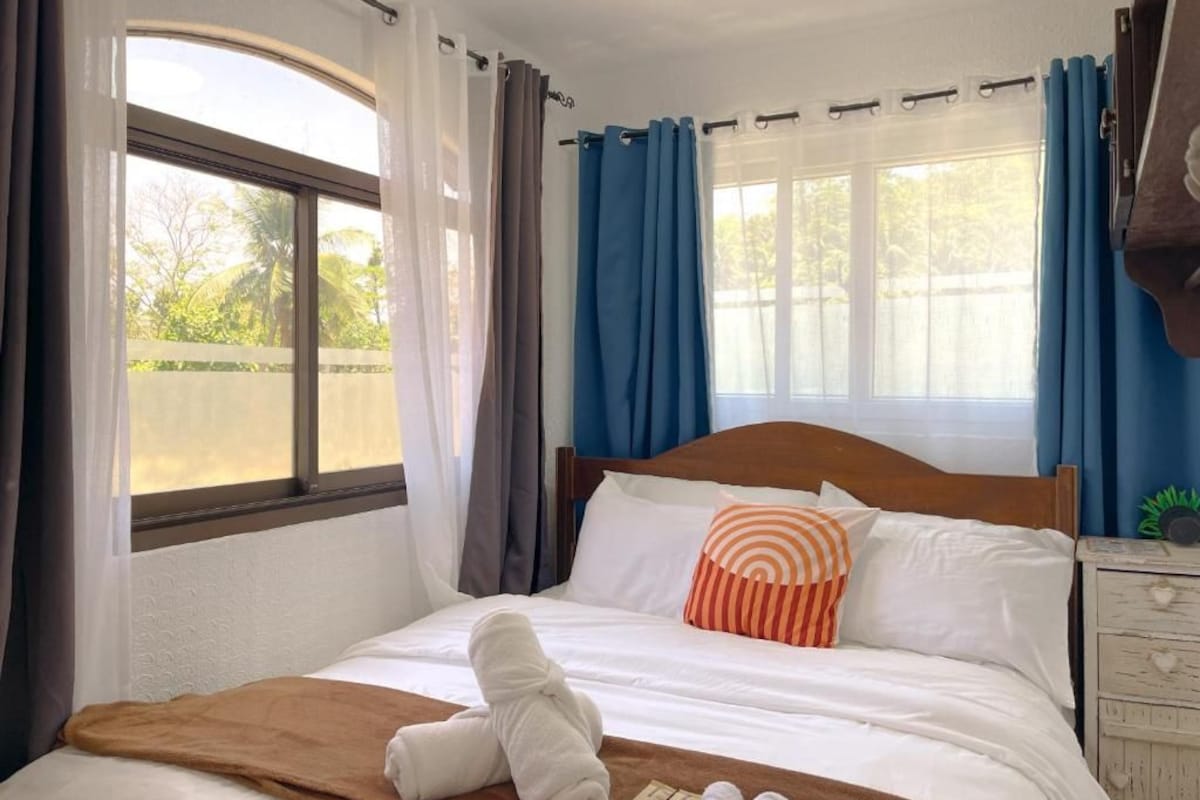 A hotel room with a bed, a window, curtains, and a wooden headboard.