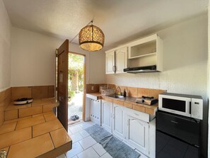 A compact kitchen with white cabinets, a microwave, a sink, and a hanging light fixture.