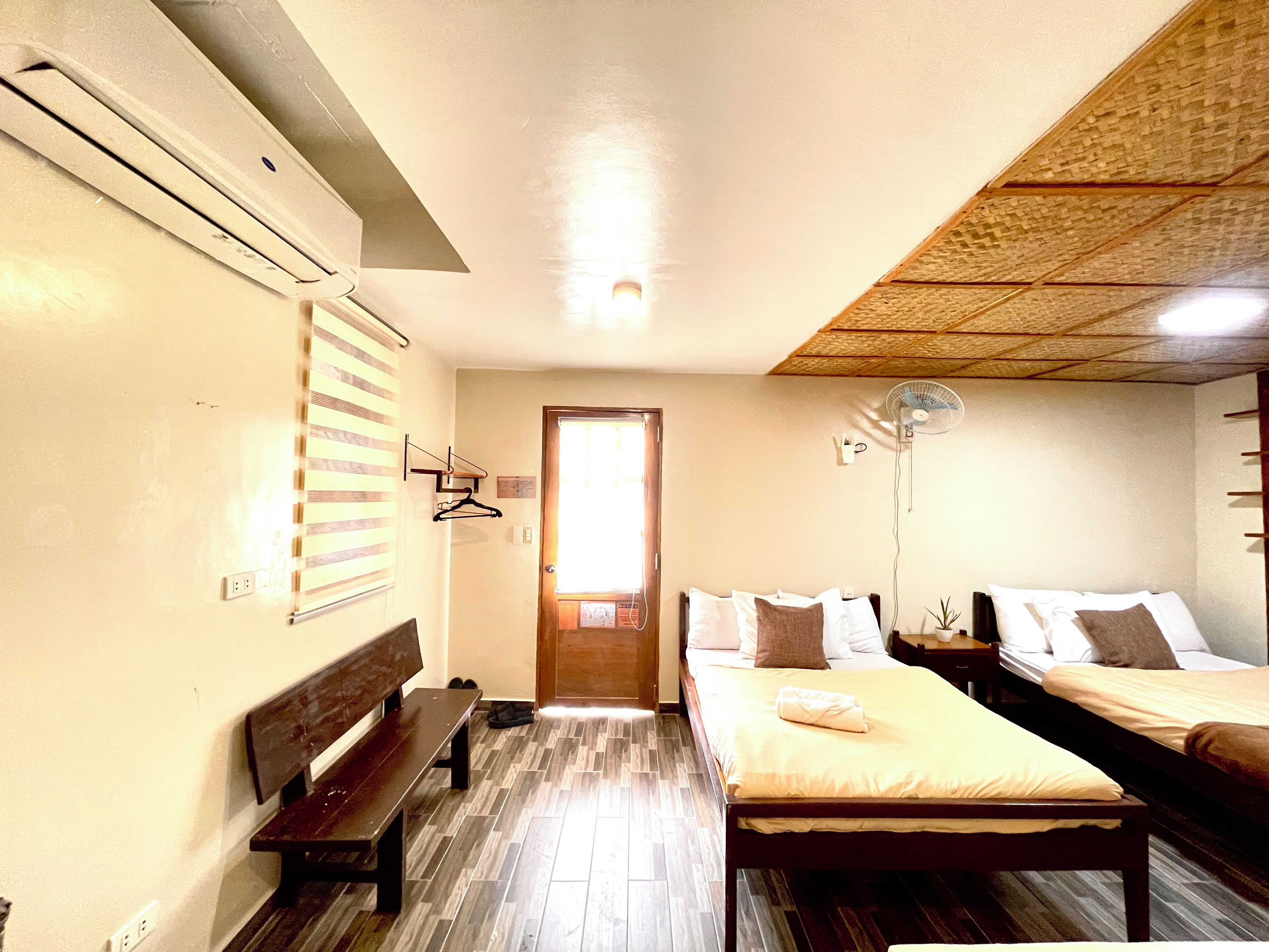 Ein Zimmer mit zwei Betten, einer Bank, einem Wandheizkörper und einem Deckenventilator.
