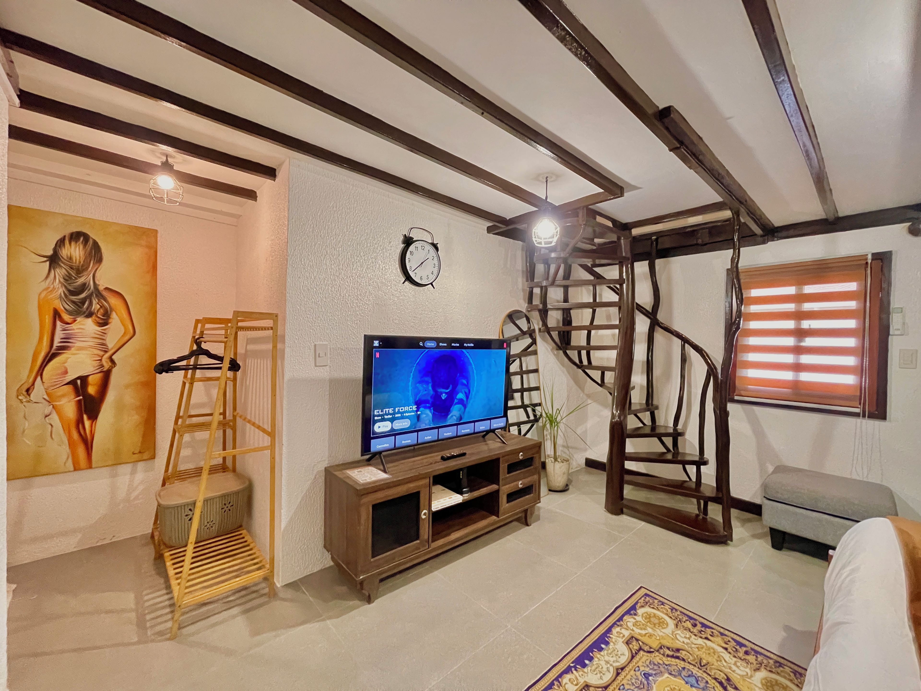 Un salon avec une télévision, un tableau, une échelle en bois, un escalier et une horloge au mur.