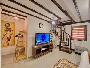 Una sala de estar con una televisión, un cuadro, una escalera de madera, una escalera y un reloj en la pared.