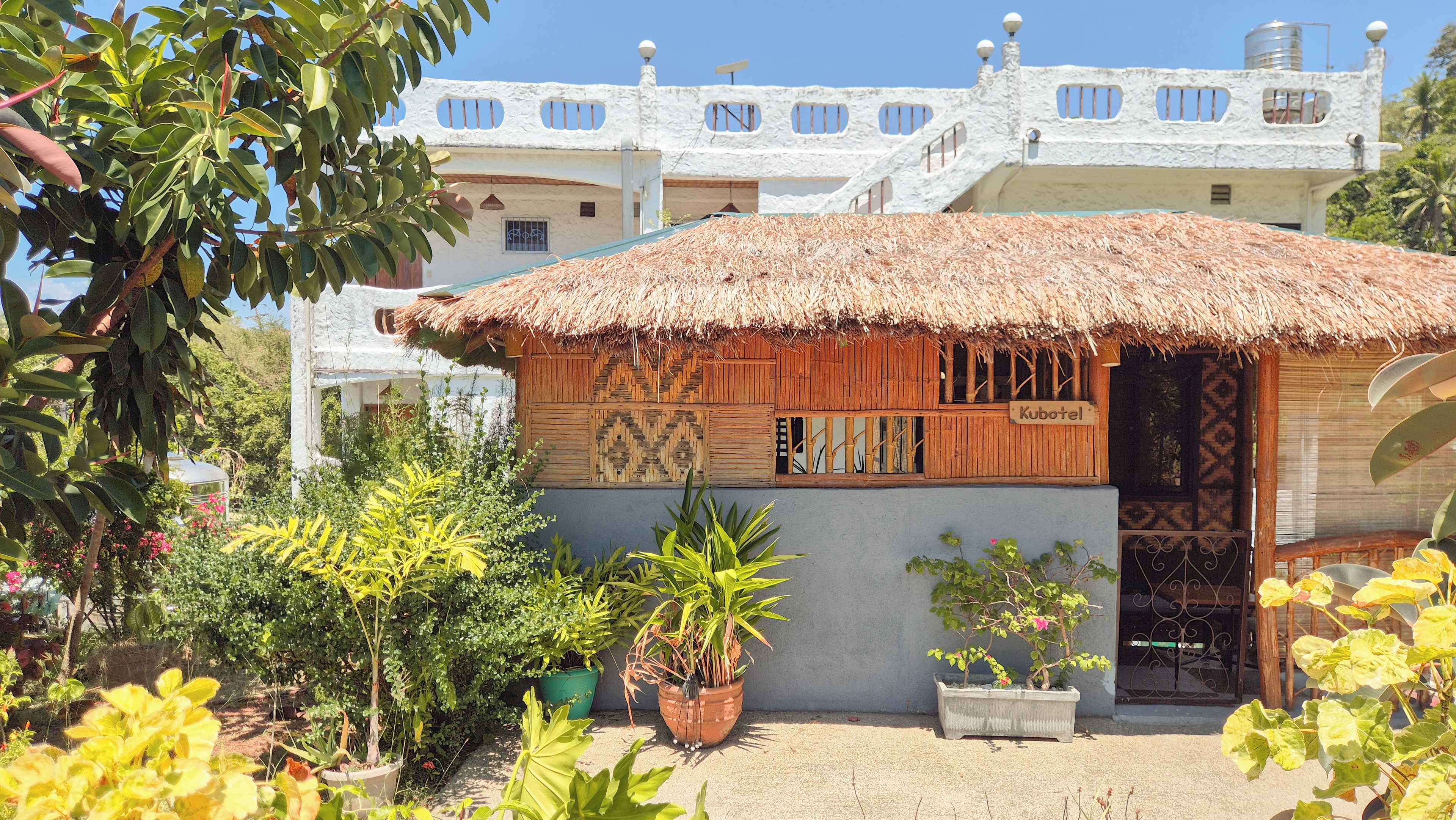 A traditional hut with a thatched roof, surrounded by potted plants and a garden.
