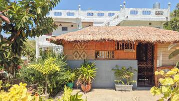 A traditional hut with a thatched roof, surrounded by potted plants and a garden.