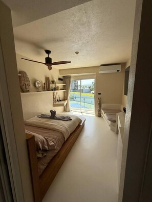 Une chambre à coucher avec un lit, un ventilateur de plafond, une fenêtre avec des rideaux et une vue sur l’extérieur.