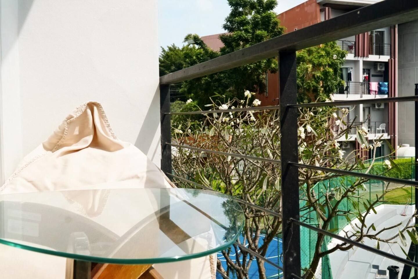 A glass table with a white object on it, a metal railing, and a view of a building with balconies and greenery.