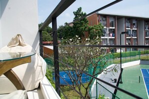 Un balcon avec une table en verre, un court de tennis et, au fond, un immeuble doté de nombreux balcons.